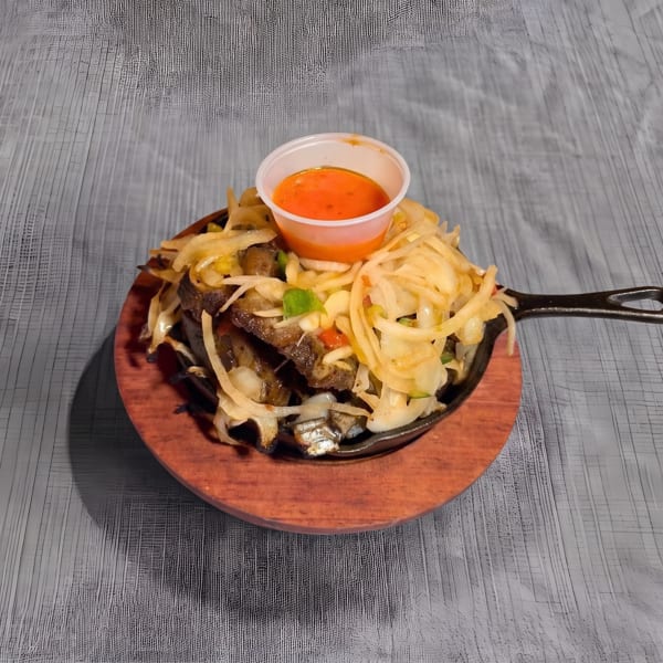 Sizzling meat and onions in a cast iron skillet with a side of orange sauce.