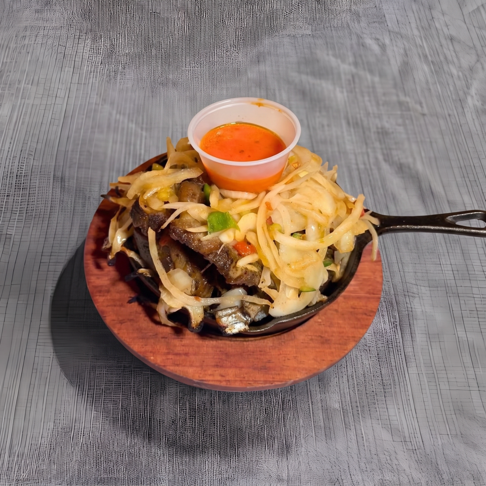 Sizzling meat and onions in a cast iron skillet with a side of orange sauce.