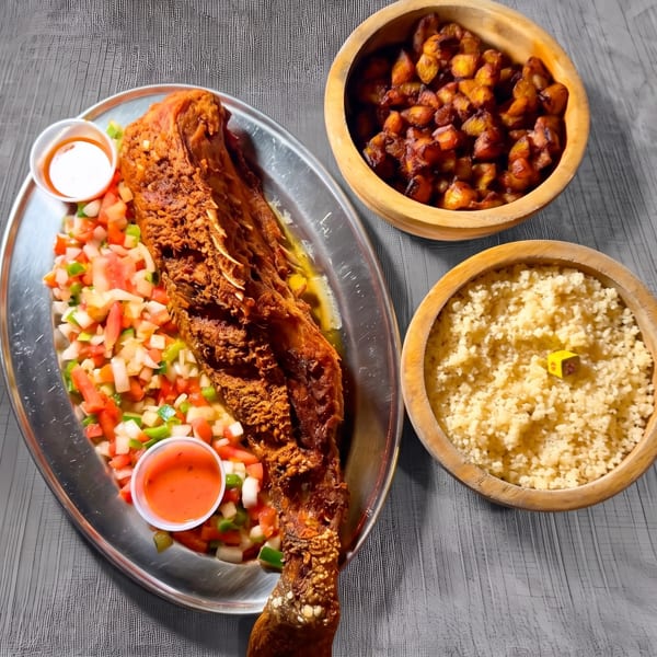A whole fried fish with a side of diced salad, couscous, and fried plantains.