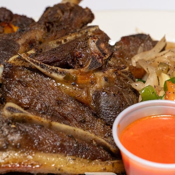 Grilled lamb chops with sautéed onions, peppers, and a side of red dipping sauce.