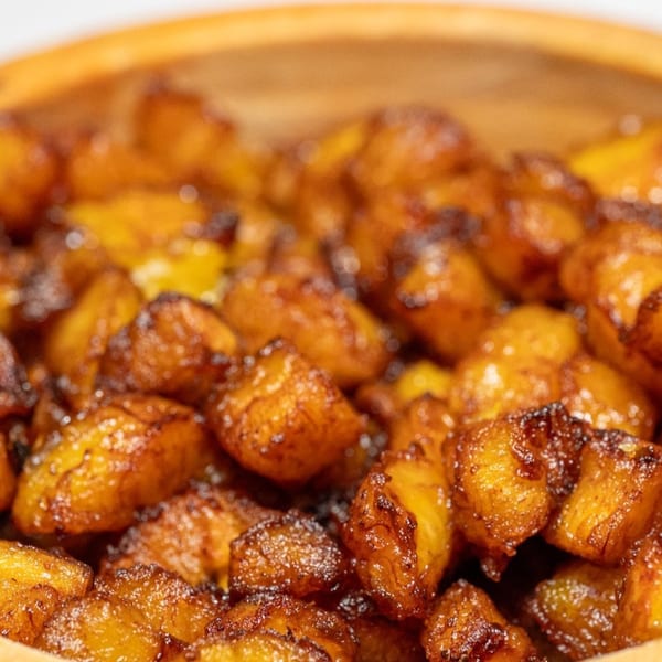 Close-up of golden brown fried plantain pieces in a light wooden bowl.